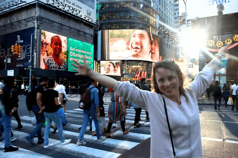 Frau freut sich auf dem Times Square in New York, umgeben von Menschen und leuchtenden Werbetafeln