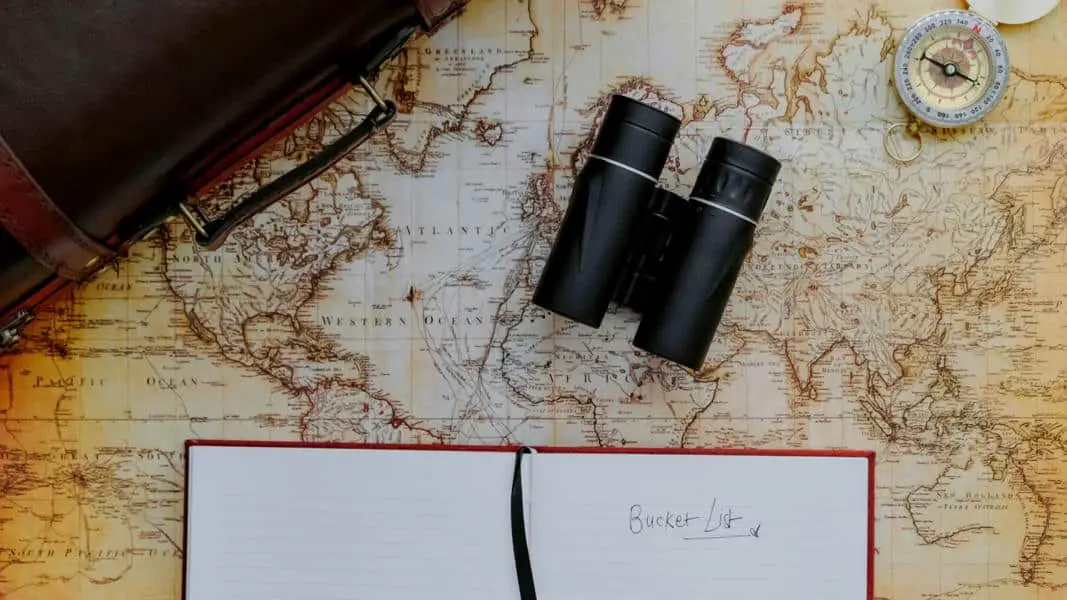 Antike Weltkarte mit Kompass, Fernglas und aufgeschlagenem Notizbuch, auf dem das Wort "Bucket List" steht