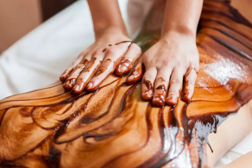 Schokoladenmassage: Zwei Hände massieren flüssige Schokolade auf einem Rücken ein