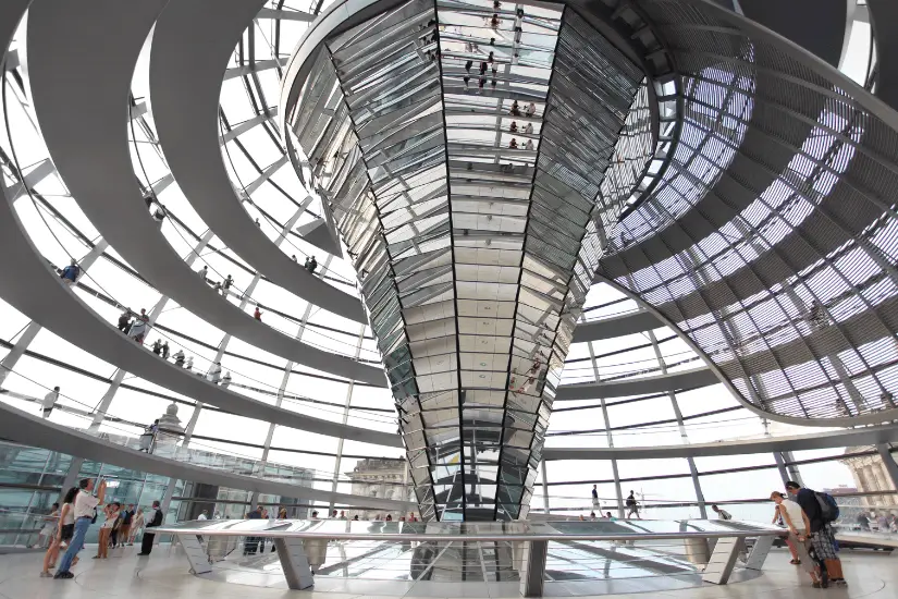 Innenansicht der Reichstagskuppel in Berlin mit Besuchern auf den spiralförmigen Gehwegen und dem modernen Glasdach.