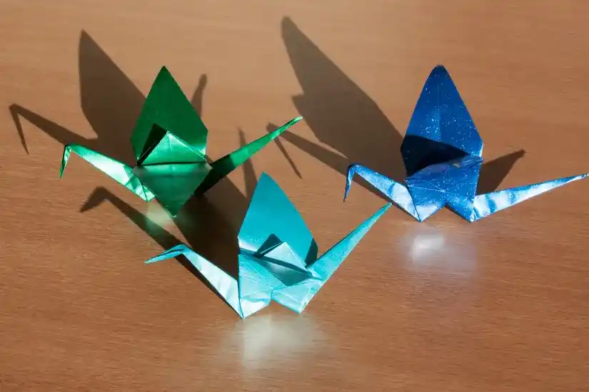 Drei bunte Origami-Kraniche auf einer Holzoberfläche