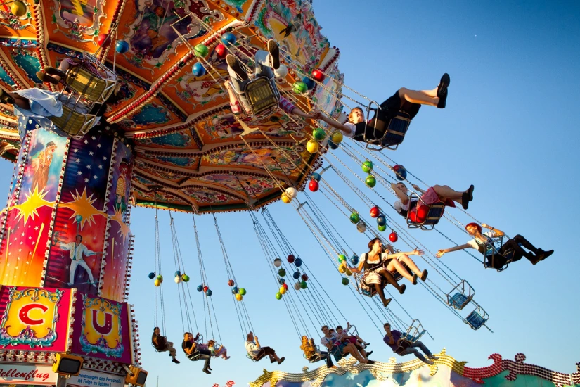 Buntes Kettenkarussell auf dem Oktoberfest mit Menschen, die bei blauem Himmel fahren.