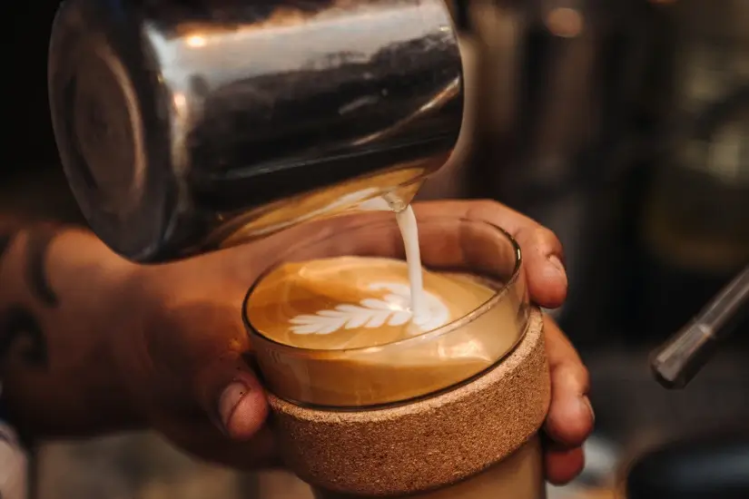 Barista gießt Milchschaum in ein Glas mit Latte Art in einem Café