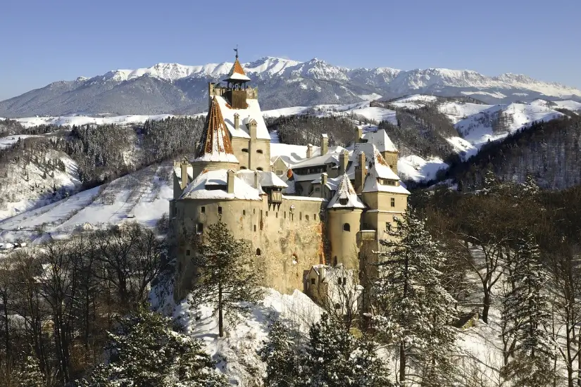 Verschneites Schloss in bergiger Winterlandschaft mit schneebedeckten Bäumen und Bergen im Hintergrund