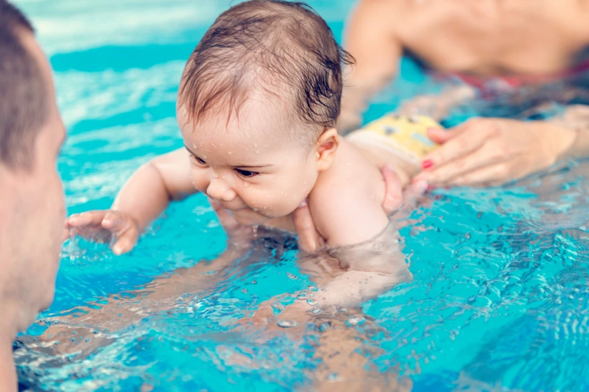 Ein Baby im Schwimmbad wird von einem Erwachsenen gehalten