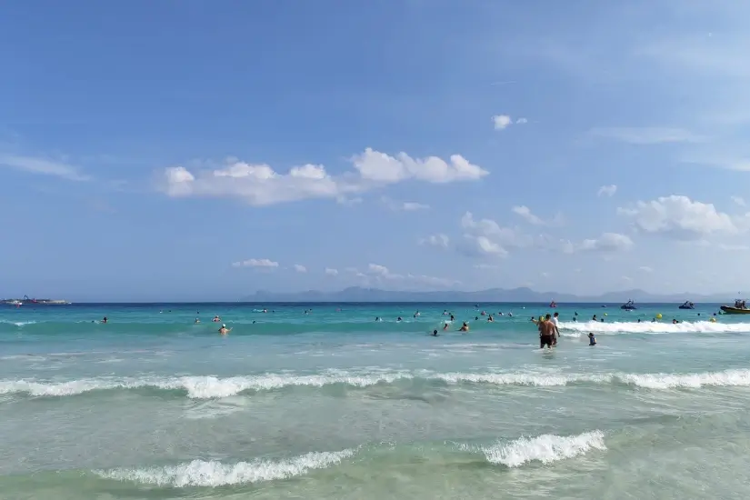 Meine Deep-Tissue-Massage-Erfahrung: Heftig, aber hilfreich? 4 strand alcudia Türkisfarbenes Meer mit Wellen und Badegästen am Strand von Alcúdia auf Mallorca